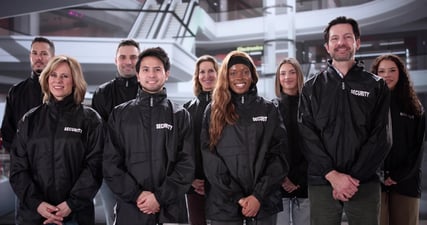 Nine shopping mall security officers pose for a group portrait in front of staircases in an empty shopping mall.