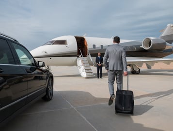 A business executive walks toward a private jet carrying a suitcase. A security professional stands by the jet. 